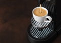 Pouring fresh morning coffee from home espresso machine to white cup on brown background Royalty Free Stock Photo