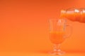 Pouring a fresh smoothie from a bottle into a glass on an orange background Royalty Free Stock Photo