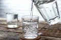 Pouring of fresh water from jug into glass on wooden table Royalty Free Stock Photo