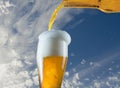 Pouring glass of beer from bottle on sky background Royalty Free Stock Photo