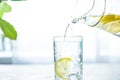 Pouring a glass of water with lemon, ice and mint on a white table