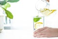 Pouring a glass of water with lemon, ice and mint on a white table Royalty Free Stock Photo