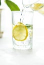 Pouring a glass of water with lemon, ice and mint on a white table Royalty Free Stock Photo