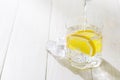 Pouring a glass of water with lemon and ice on a white table. Homemade lemonade with lemons slices Royalty Free Stock Photo