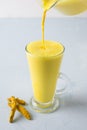 Pouring golden turmeric milk in latte glass. Natural detox beverage. Close up. Vertical shot