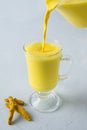 Pouring golden turmeric milk in latte glass. Natural detox beverage. Close up. Vertical shot