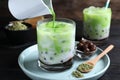 Pouring green matcha into glass with milk bubble tea at black wooden table, closeup