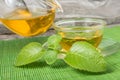 Pouring green tea into cup with mint leaves.