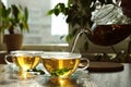 Pouring green tea into glass cup with saucer and leaves on wooden table Royalty Free Stock Photo