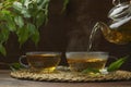 Pouring green tea into glass cup with saucer and leaves on wooden table Royalty Free Stock Photo