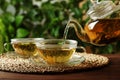 Pouring green tea into glass cup with saucer on wooden table Royalty Free Stock Photo