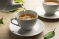 Pouring green tea into white cup with saucer and leaves on wooden table, closeup Royalty Free Stock Photo