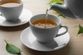 Pouring green tea into white cup with saucer and leaves on wooden table, closeup Royalty Free Stock Photo