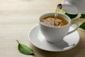 Pouring green tea into white cup with saucer and leaves on wooden table, closeup. Space for text Royalty Free Stock Photo