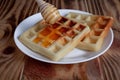 Pouring honey on Belgian or Viennese waffles on white plate on wooden table using honey dipper