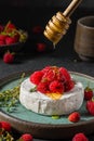 Pouring honey on brie or camembert cheese with wild berries and thyme on dark background