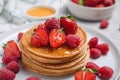 Pouring honey onto tasty pancakes with fresh berries on plate, closeup Royalty Free Stock Photo