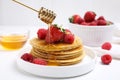 Pouring honey onto tasty pancakes with fresh berries on white table Royalty Free Stock Photo