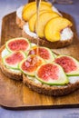 Pouring honey on toasts with cream cheese topped with fresh ripe figs and peaches. Wholegrain rye bran bread on wood cutting board