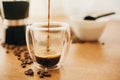 Pouring hot coffee in glass cup on background of roasted coffee beans, grounded coffee, geyser coffee maker on wooden table. Royalty Free Stock Photo