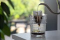 Pouring hot water into glass with drip coffee bag from kettle on light grey table, closeup. Space for text Royalty Free Stock Photo