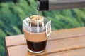 Pouring hot water into glass with drip coffee bag from thermos on wooden table, closeup Royalty Free Stock Photo