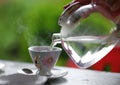 Pouring hot water from glass teapot into the tea cup, summer outdoor. Royalty Free Stock Photo