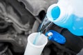 Pouring liquid from plastic canister into car washer fluid reservoir. Close up filling windscreen water tank with washing liquid