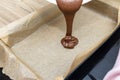 Pouring a liquid thick mass of cocoa dough onto a baking sheet lined with baking paper. Royalty Free Stock Photo