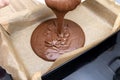 Pouring a liquid thick mass of cocoa dough onto a baking sheet lined with baking paper. Royalty Free Stock Photo