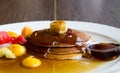 Pouring maple syrup on three pancakes with butter and fruits white plate
