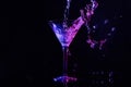 Pouring martini. Glass and splashes in neon lights on dark background Royalty Free Stock Photo