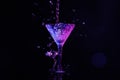 Pouring martini. Glass and splashes in neon lights on dark background, bokeh effect Royalty Free Stock Photo