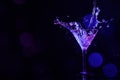 Pouring martini. Glass and splashes in neon lights on dark background, bokeh effect with space for text Royalty Free Stock Photo