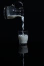 Pouring milk from a bottle to the glass on the black backround