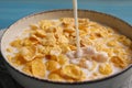 Pouring milk into bowl of tasty corn flakes at light blue table, closeup Royalty Free Stock Photo