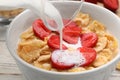 Pouring milk into bowl of tasty crispy corn flakes with strawberries at table Royalty Free Stock Photo