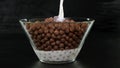 Pouring milk and chocolate cereal balls into a glass bowl on black background. Close up. Royalty Free Stock Photo