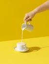 Pouring milk in a cup, on yellow background. Milk overflow from a cup