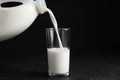 Pouring milk from gallon bottle into glass on black table Royalty Free Stock Photo