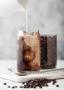 Pouring milk into glass with iced black coffee with glass container of beans and spoon on marbel board and light background Royalty Free Stock Photo