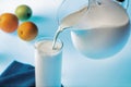 Pouring milk from glass jug into glass on blue Royalty Free Stock Photo