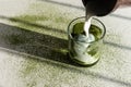 Pouring milk into glass with matcha green tea ice on white table sprinkled with matcha powder and strong shadows Royalty Free Stock Photo