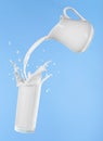 Pouring milk from jug into glass cup  with splashing on blue background Royalty Free Stock Photo
