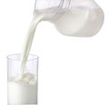 Pouring milk from jug into glass isolated on white background Royalty Free Stock Photo