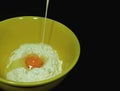 Pouring milk into raw flour and egg yolk in yellow ceramic mixing bowl on black background, with free space for design Royalty Free Stock Photo