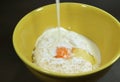 Pouring milk into yellow ceramic mixing bowl with dry flour and egg for making pancakes Royalty Free Stock Photo