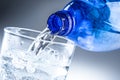 Pouring mineral water from blue bottle into clear glass on abstract grey background Royalty Free Stock Photo