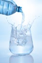 Pouring mineral water and splashing from bottle into glass on blue background. Vertical format Royalty Free Stock Photo