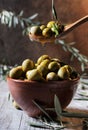 Pouring oil on wooden spoon with olives over a filled bowl